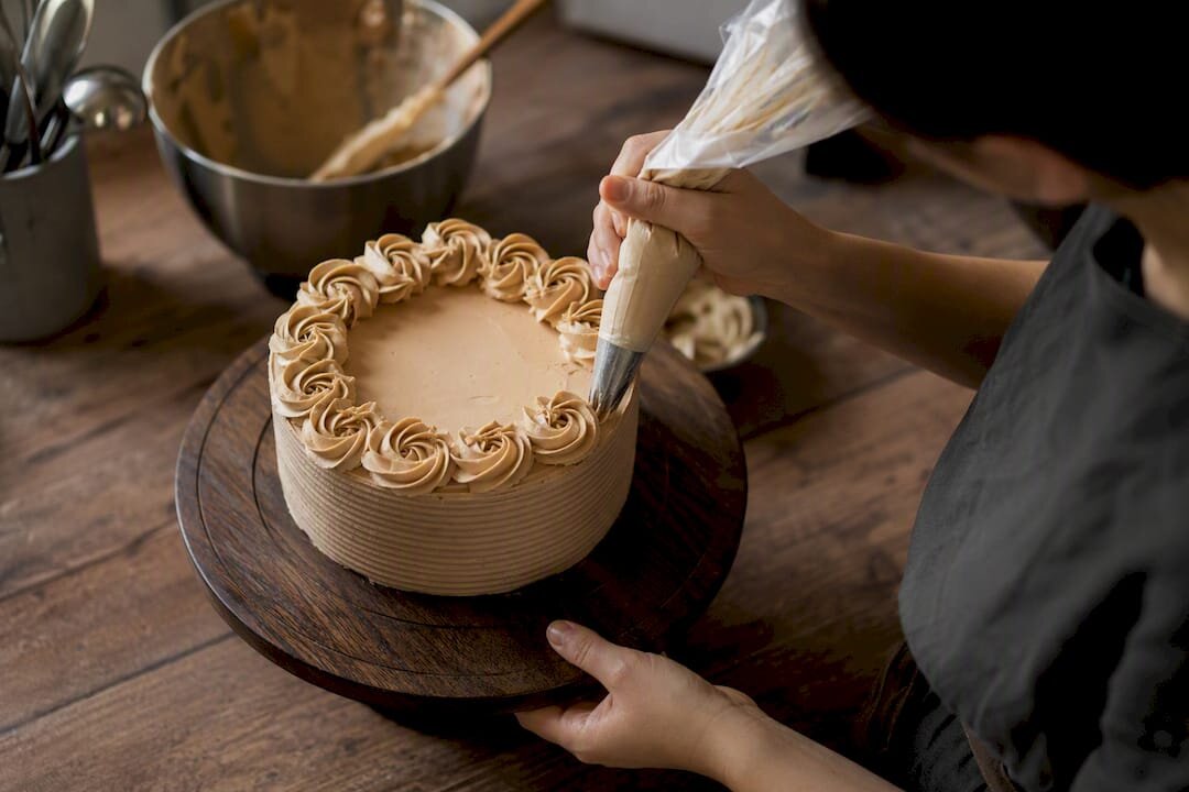 Hände, die Rosetten auf einen Kuchen auf einem Drehteller spritzen
