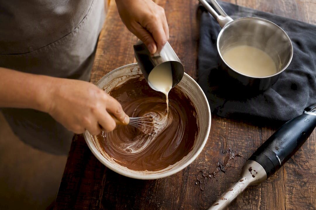 Hände, die mit Sahne und einem Schneebesen eine geronnene Ganache wieder in Form bringen