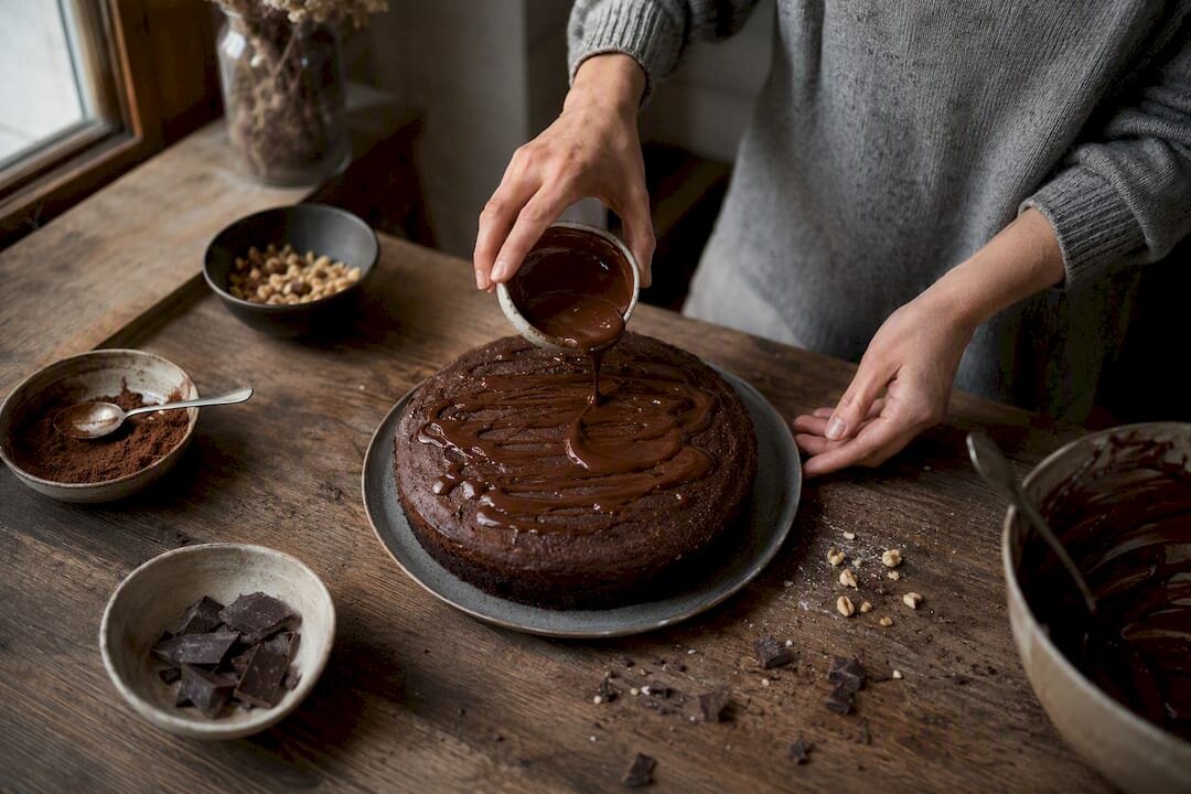Hände, die einen Schokoladenkuchen mit Kakaopulver verzieren